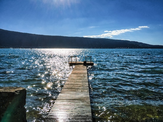Lac d'Annecy, Menthon Saint Bernard, France - July 03, 2016: High contrast of the sun we see a jetty with people sitting on it, calm and enjoying the sun @ credit Depositphotos