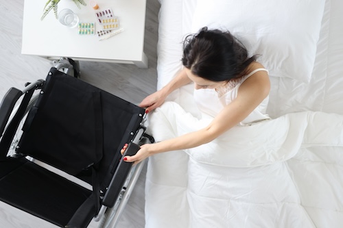 Disabled woman gets out of bed and holds onto wheelchair @ credit Depositphotos