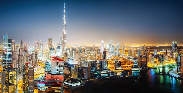 Aerial panorama view of a big futuristic city by night. Business bay, Dubai, United Arab Emirates. Colorful nighttime skyline. @ credit Depositphotos