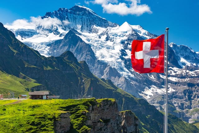Swiss flag wavingon a Mannlichen viewpoint with peak of Jungfrau mountain on the background, Bernese Oberland Switzerland @ credit Depositphotos