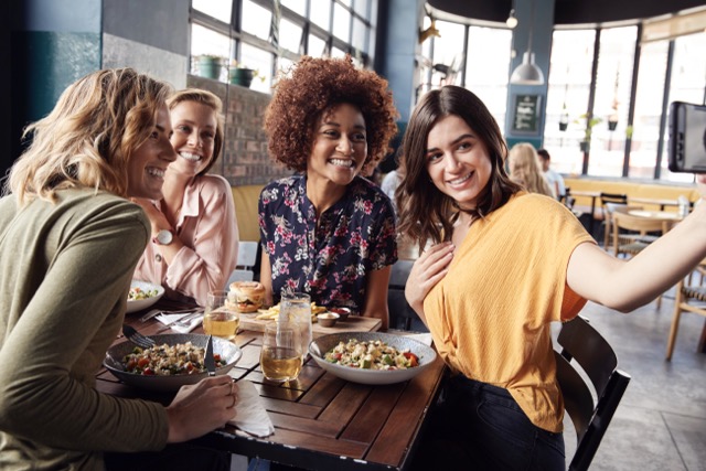 Four Young Female Friends Meeting For Drinks And Food Posing For Selfie In Restaurant