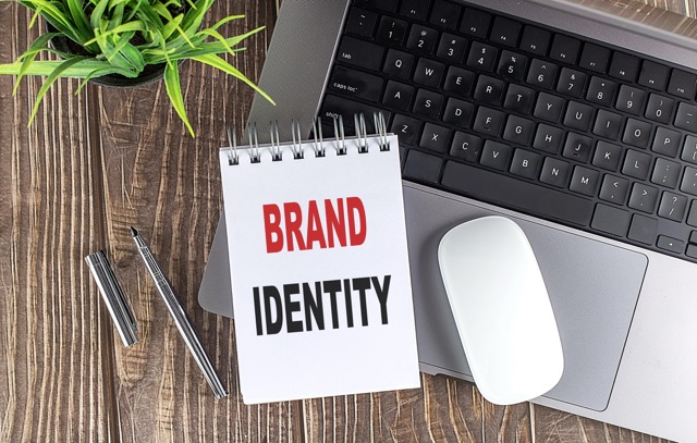 Laptop, mouse and notebook notes with text BRAND IDENTITY on wooden background.