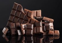 Patrimoine 🇫🇷 | Elior acquiert la chocolaterie Pailhasson et contribue à préserver le patrimoine gastronomique ! Broken bitter and milk chocolate bars on a black reflective background. Copy space.