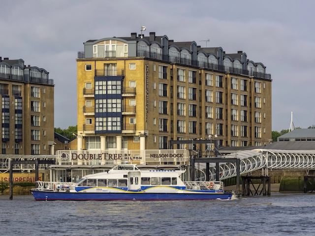 LONDON, UK - JULY 04, 2018: Thames Clipper river bus in front of DoubleTree by Hilton Hotel on Docklands Riverside @ credit Depositphotos.com