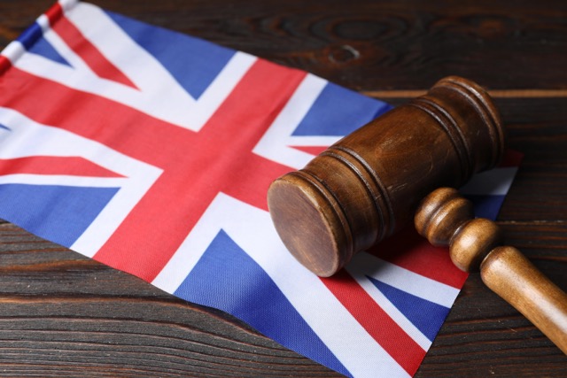 Judge's gavel and flag of United Kingdom on wooden table, closeup