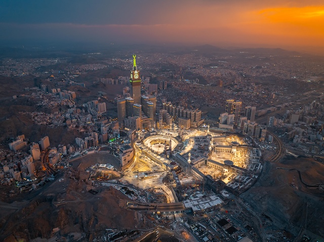 Aerial view at night of the illuminated Grand Mosque and Abraj Al-Bait Clock Tower in Mecca, showcasing the city’s vibrant glow as lights shimmer across the holy site @ credit Depositphotos.com